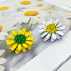 Detail von weißen und gelben Gänseblümchen-Broschen auf floralem Hintergrund