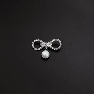 Detailed view of an elegant silver bow brooch with sparkling rhinestones and a hanging pearl.