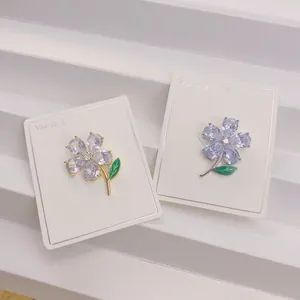 Nahaufnahme eleganter Blumenbroschen mit Zirkon-Blütenblättern und grünen Emaille-Blattdetails