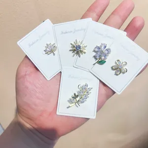 Verschiedene elegante Kupfer-Broschen mit Zirkonia-Steinen auf weißen Displaykarten
