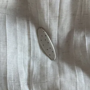 Detail view of cream white polka dot snap hair clip on textured pleated fabric