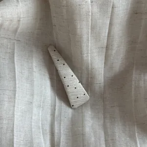 Macro detail of white textured polka dot triangle hair clip on pleated fabric