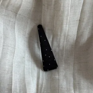 Close-up of a black triangular hair clip with white polka dots on pleated fabric.
