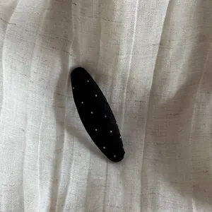 Close-up detail of a classic black hair clip with white polka dots on linen fabric