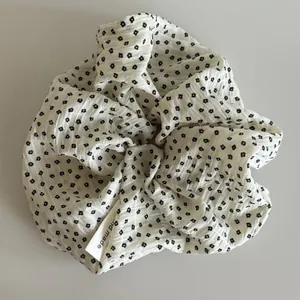 Detail view of a white floral scrunchie with crinkled texture and hand made tag