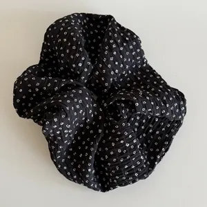 Close-up of elegant black scrunchie with white floral patterns and crinkled pleated texture