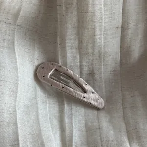 Detailed view of a light pink polka dot snap hair clip on pleated linen fabric