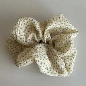 Close-up view of a cream fabric scrunchie featuring a delicate purple floral pattern