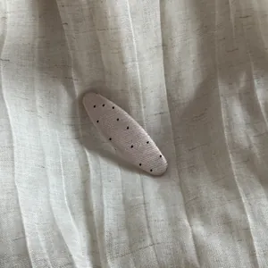 Macro detail of a pink satin hair clip featuring black polka dots on pleated background