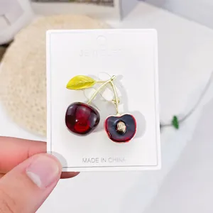 Detailed view of a cute red cherry brooch with gold stem on a white card