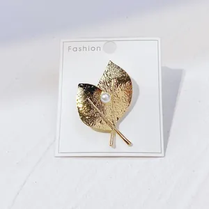 Detailaufnahme einer eleganten goldenen Blattnadel mit Perle auf einer schlichten Karte