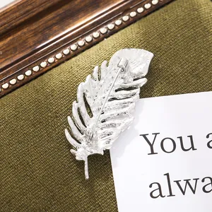 Detailed close-up of a silver feather-shaped suit pin brooch on green fabric