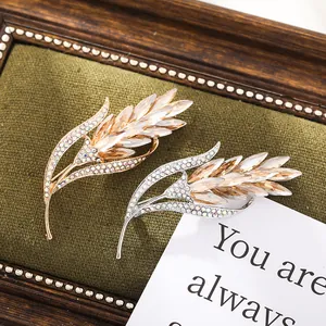 Elegant gold and silver wheat ear brooches with crystals displayed on green velvet fabric.
