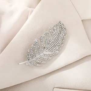 Close-up view of an elegant silver feather brooch encrusted with rhinestones on a beige blazer
