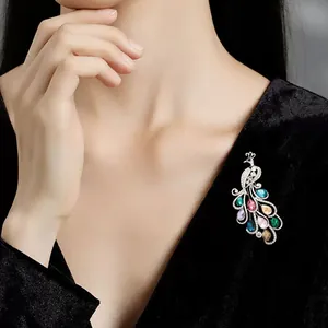 Nahaufnahme einer farbenfrohen Pfauen-Kristallbrosche auf einem eleganten schwarzen Samtkleid