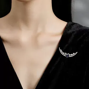 Close-up of a silver crescent moon brooch with a blue square stone on black velvet.