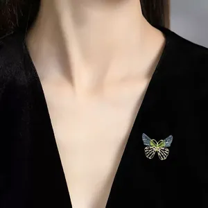 Primer plano de un elegante broche de mariposa con alas traslúcidas en vestido negro.