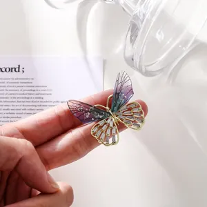 Primer plano macro que muestra las alas de resina translúcida y el broche de mariposa de cristal.