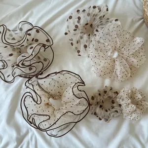 Detail view of five assorted polka dot mesh scrunchies on soft white fabric