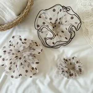 Detailed view of three different sizes of mesh polka dot scrunchies in cream and brown.