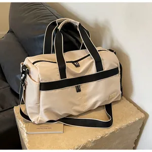 Large beige oxford cloth travel tote bag on a stone pedestal with a black sofa.