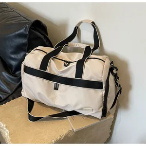 Angle view of beige oxford travel duffle bag with black straps on stone base