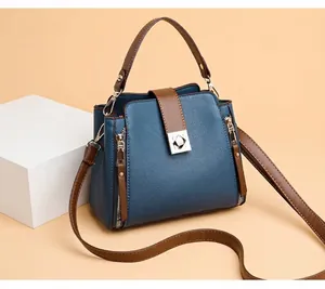 Bolso de hombro tipo cubo en cuero azul con correas marrones y detalles dorados
