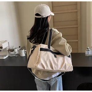 Detail view of a large beige Oxford cloth travel tote bag worn by a model in a cafe.