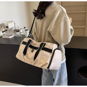 Detail of large beige Oxford travel bag carried by a model in a cafe setting.