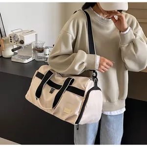 Model carrying a beige large capacity Oxford travel duffel bag with black straps