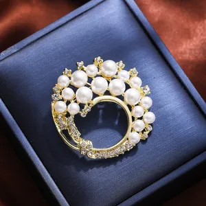 Elegant circular gold brooch with white pearls and sparkling rhinestones on blue box
