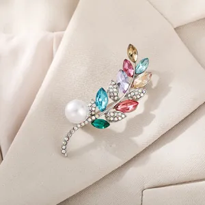 Detailansicht einer eleganten bunten Kristall-Zweig-Brosche mit Perle an einem beigen Revers.