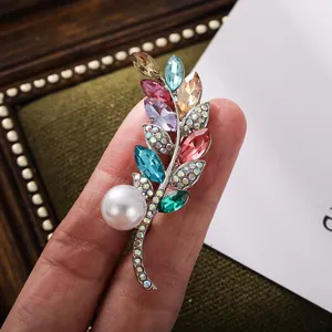 Nahaufnahme einer Blattbrosche mit bunten Kristallen und einer eleganten Perle.