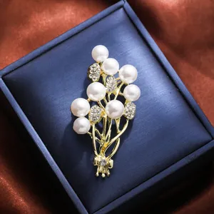 Elegant gold floral bouquet brooch with white pearls and rhinestones on a blue box