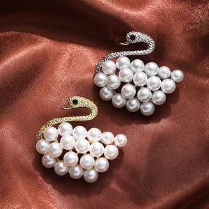 Elegant pearl swan-shaped brooches in gold and silver tones on brown satin fabric.