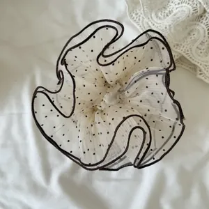 Detail showing the sheer mesh texture and black polka dot pattern of the scrunchie.