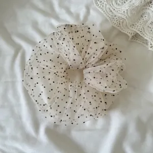 Macro detail view of a soft off-white mesh scrunchie with classic black polka dots