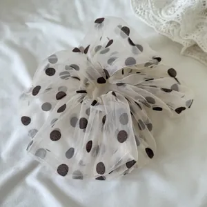 Detail view of a cream mesh scrunchie with brown polka dots for soft hair styling.