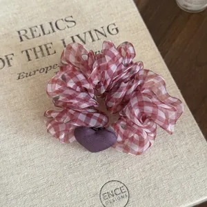 Close-up of pink gingham scrunchie with purple heart charm on vintage book.
