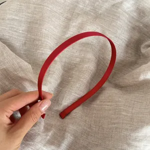 Primer plano de una fina diadema de satén rojo vibrante sostenida a mano sobre tela de lino.