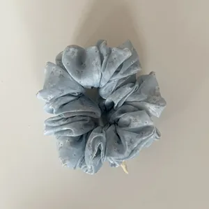 Detail view of a light blue floral chiffon scrunchie with delicate white flower patterns