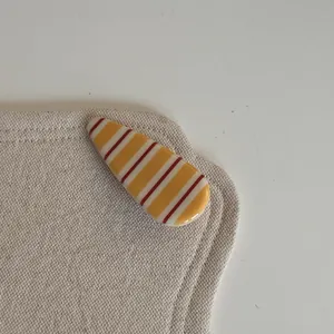Vue détaillée montrant la texture brillante d'une pince à cheveux rayée jaune et rouge