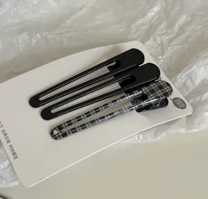 Detail view of three minimalist black and plaid hair clips on a white display card.