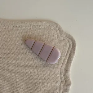 Vue rapprochée d'une pince à cheveux rose minimaliste avec des rayures marron sur un tapis.