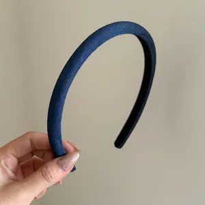 Nahaufnahme eines schmalen Retro-Haarreifens aus Denim-Stoff in der Hand zur Größe