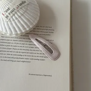 Close-up detail of a minimalist pink faux leather BB hair clip on a vintage book page