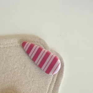 Gros plan d'une pince à cheveux rayée rose sur un tissu beige pour une esthétique minimaliste