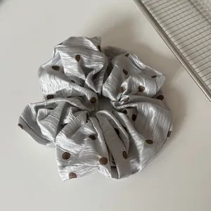 Nahaufnahme eines silbergrauen Satin-Scrunchies mit braunen Punkten und Falten