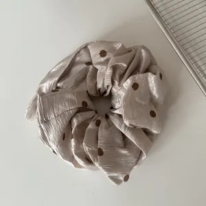 Nahaufnahme eines französischen Plissee-Scrunchies mit eleganten Punkten auf Champagnerstoff.