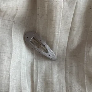 Detailed close-up showing the texture of a silver polka dot hair clip on linen fabric